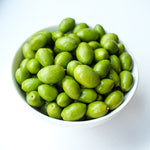 White bowl filled with green olives on a white background