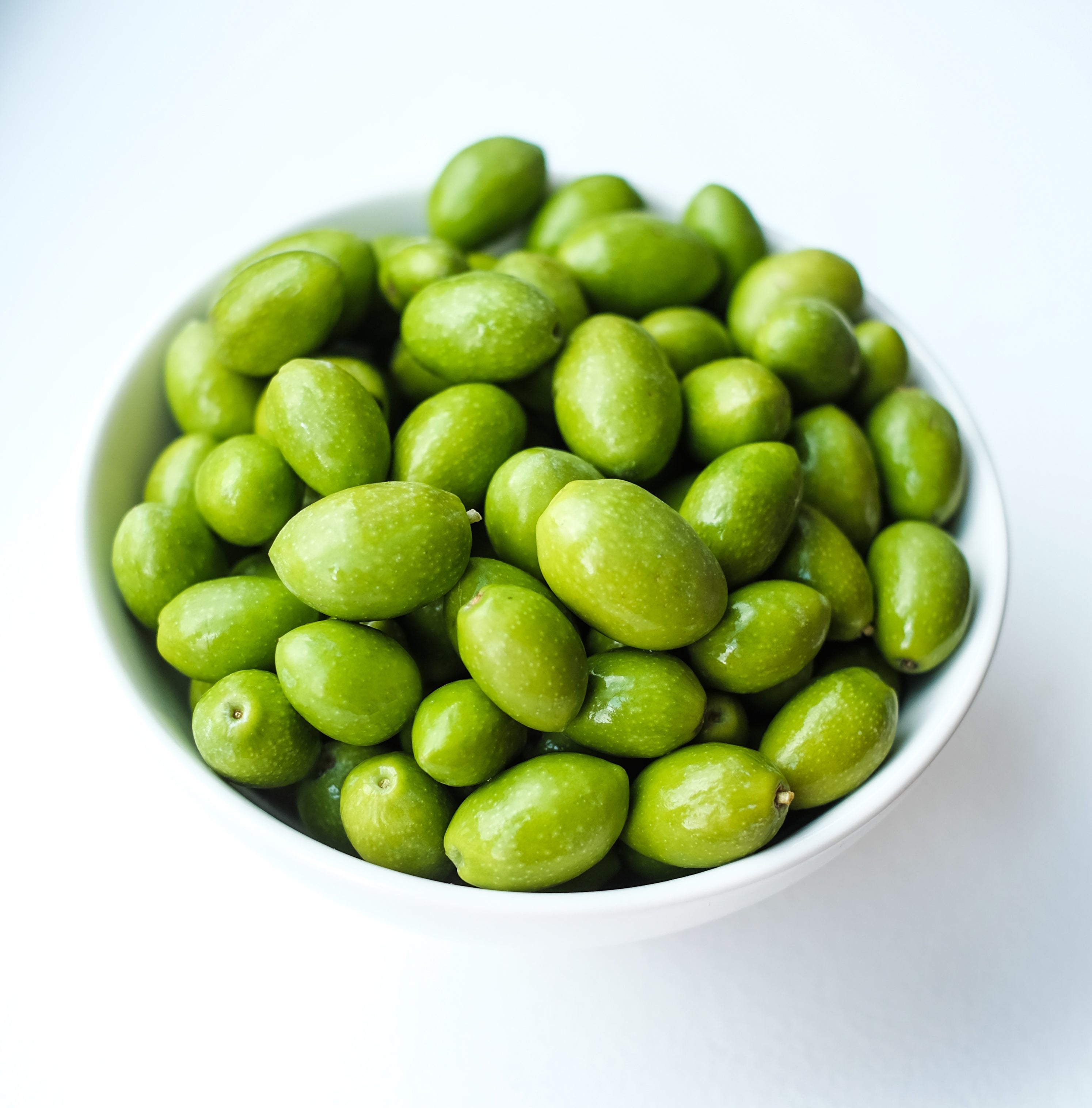 White bowl filled with green olives on a white background