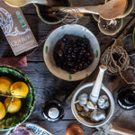 Tabletop scene with lemons, olives, and other ingredients on a wooden surface.