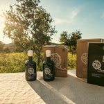 Two olive oil bottles and packaging on a table with a scenic background