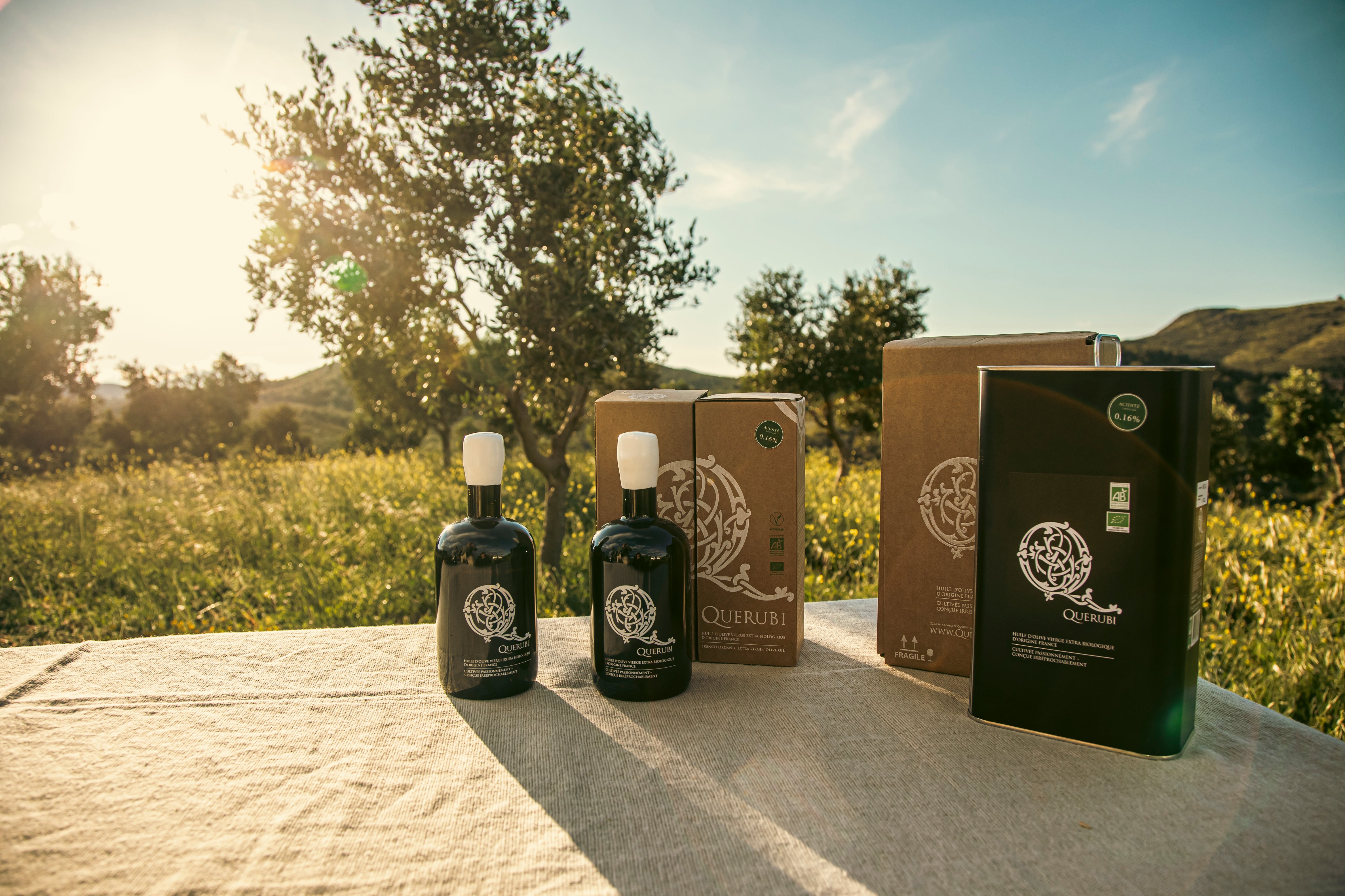 Two olive oil bottles and packaging on a table with a scenic background